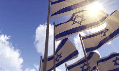 Israel flags against a blue sky with sun shining through