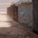 Photo of a woman walking along the beach next to the border wall in Mexico