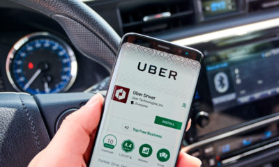Uber driver inside car with ridesharing app displayed on smartphone.