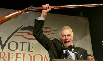 Photo of National Rifle Association President Charlton Heston holding up a rifle