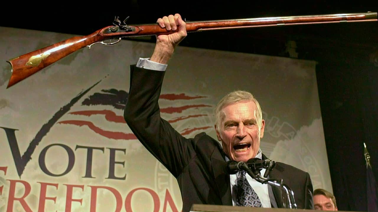 Photo of National Rifle Association President Charlton Heston holding up a rifle
