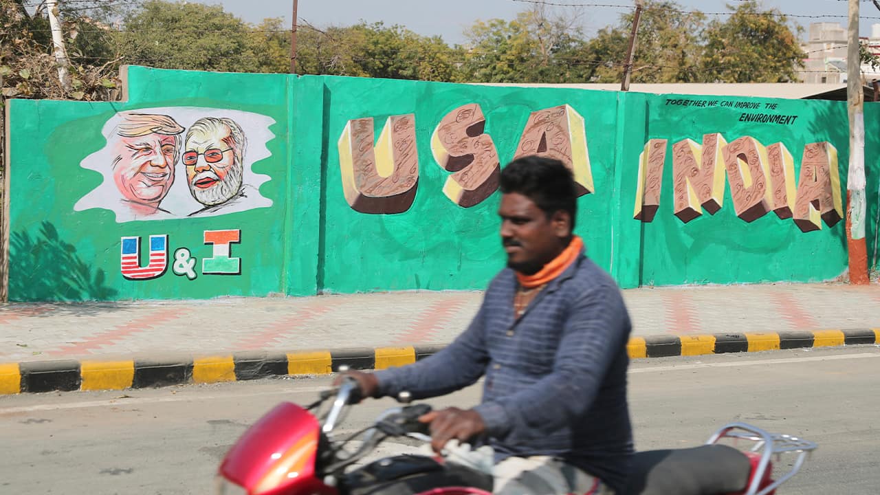Photo of a man riding past a wall with portraits of U.S. President Donald Trump and Indian Prime Minister Narendra Modi