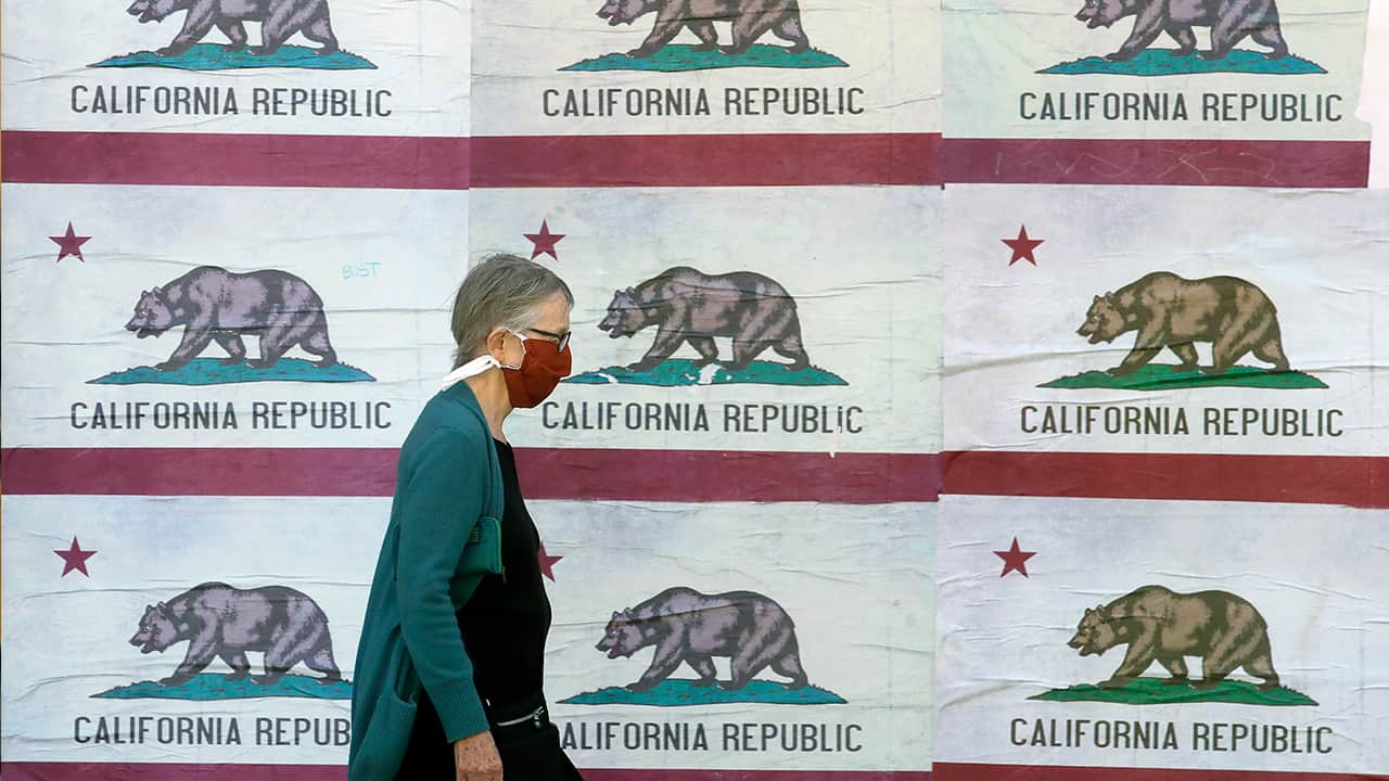 Photo of a woman wearing a mask walking past California flags